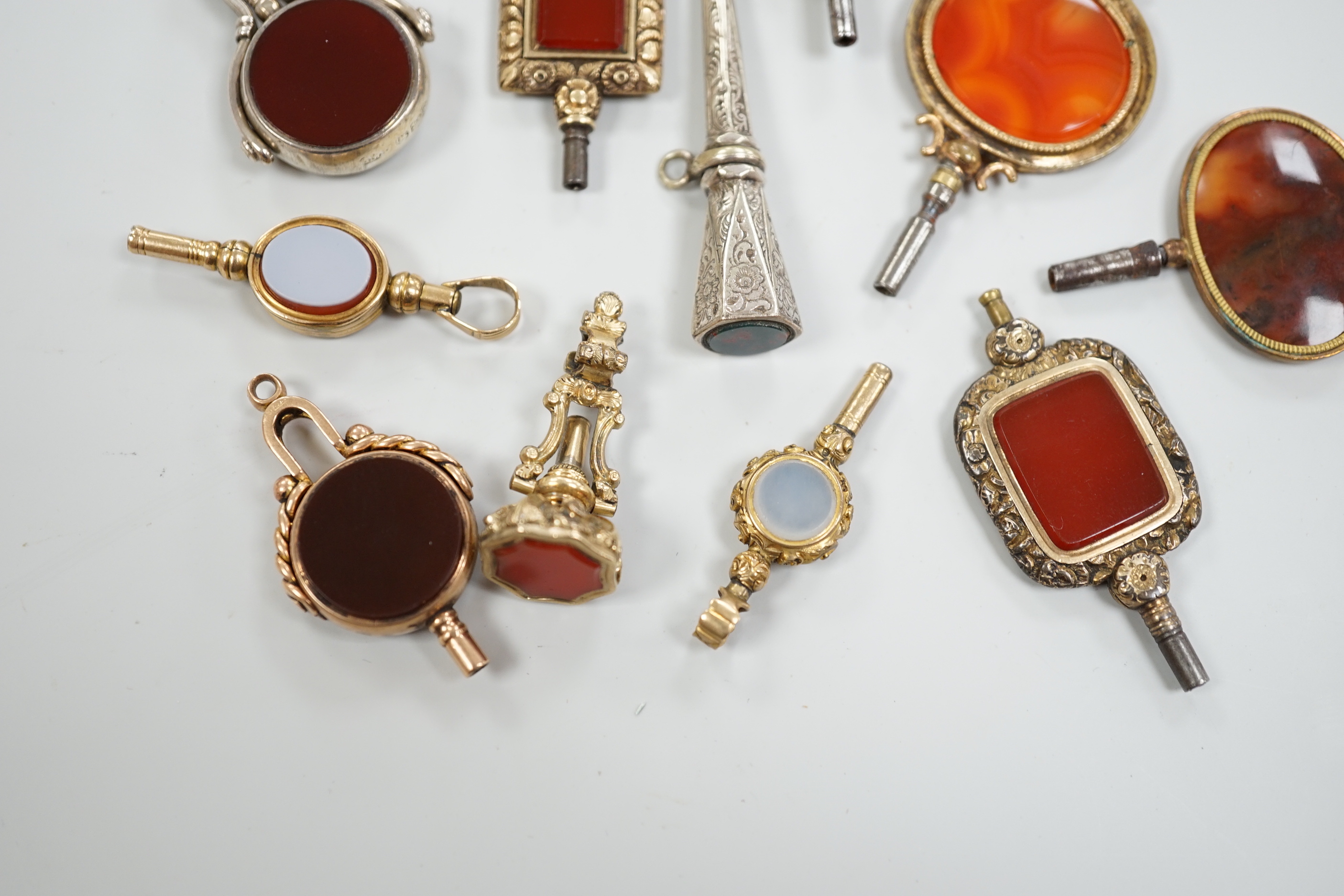 Sixteen assorted 19th century and later, 9ct gold and yellow or white metal overlaid and chalcedony set watch keys, including bloodstone, sardonyx, banded agate and moss agate and spinning fobs, largest 56mm.